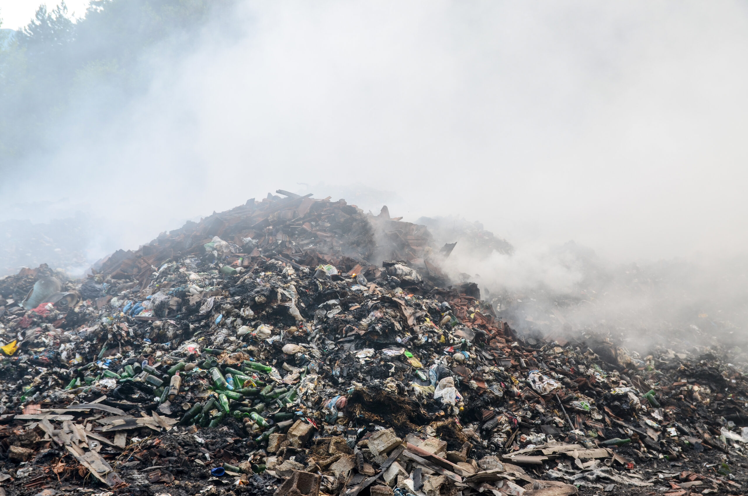 Illegal waste dump. Piles of garbage in nature. Open landfill site with burning waste. Air and environmental pollution. The smoke and smell of the landfill area pollute the air. Environment